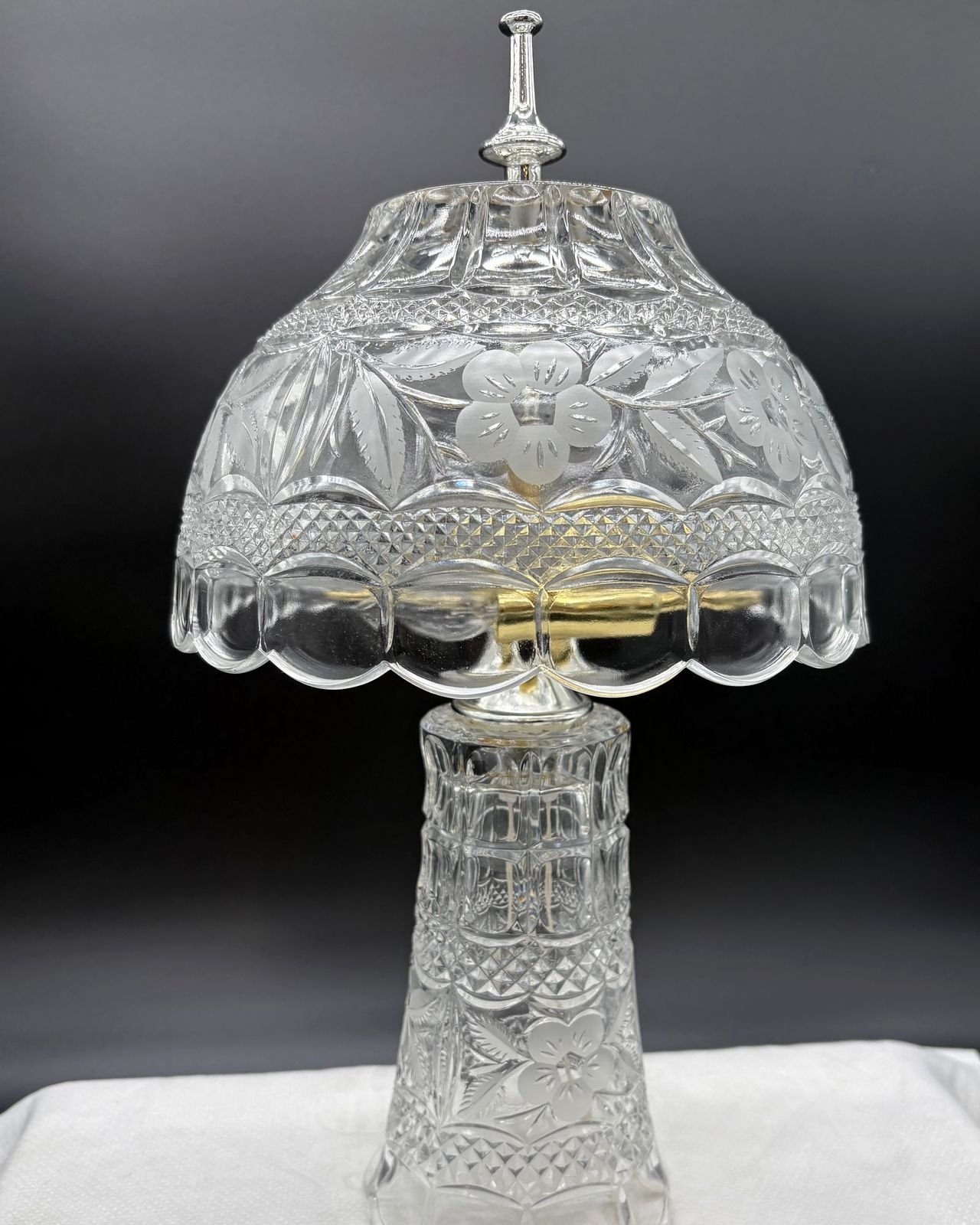 Vintage lead crystal desk lamp with a domed cut-glass shade of frosted flowers, a faceted crystal base, and a silver finial, on a white cloth.