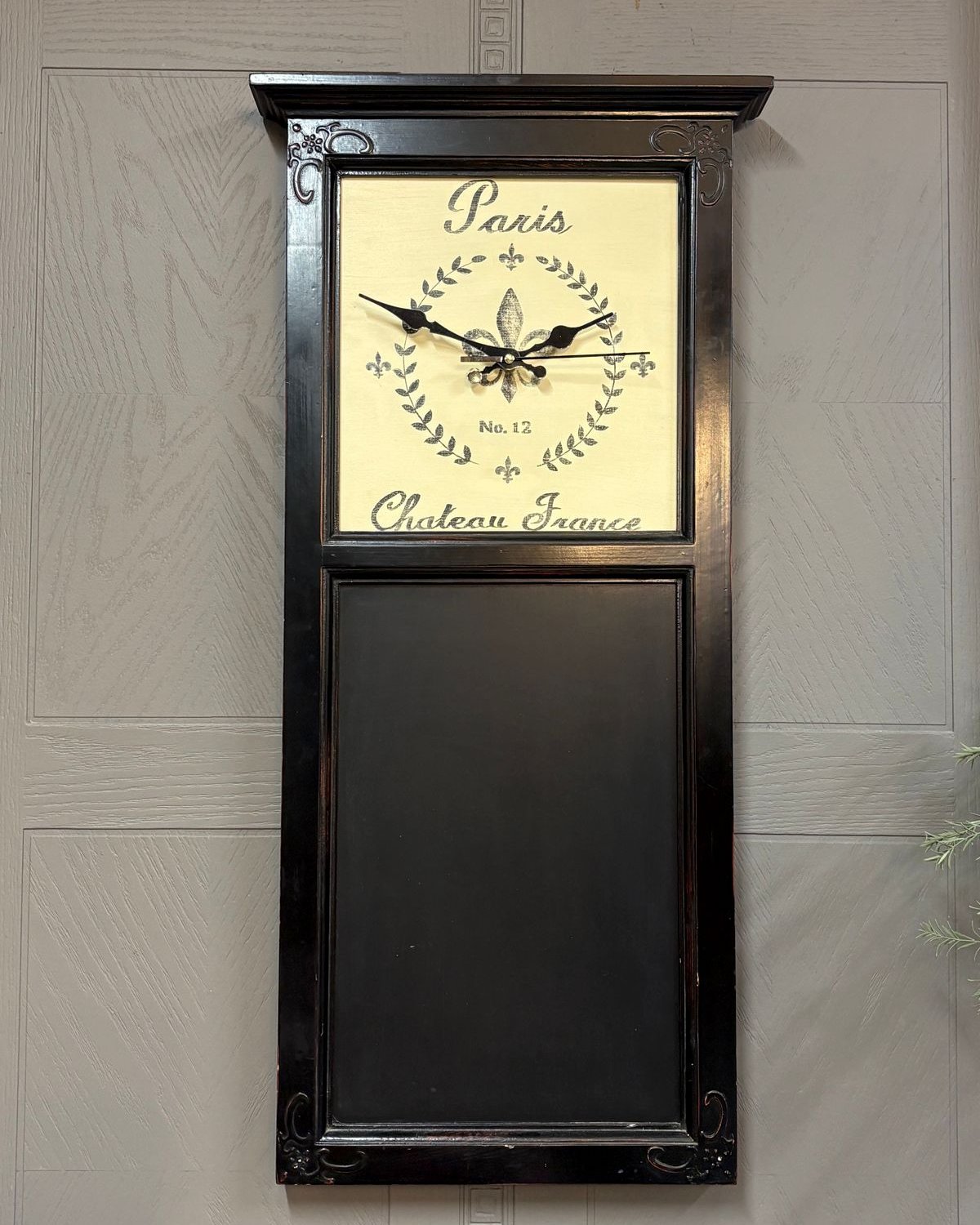 A tall black wood wall clock with a cream Paris-themed face reading Paris Chateau France, a laurel wreath and fleur-de-lis, ornate hands, and a chalkboard panel below.