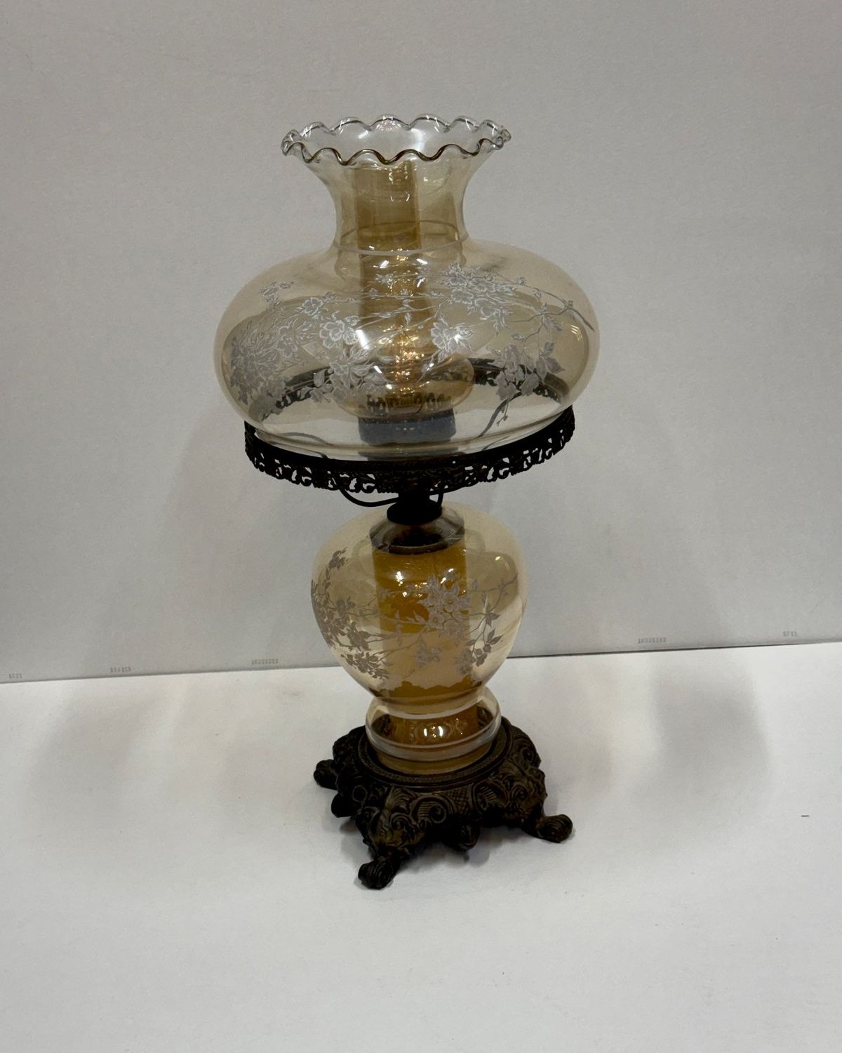 Vintage double globe hurricane table lamp with amber glass globes decorated in white flowering branches, a ruffled top rim, and an ornate dark metal base.